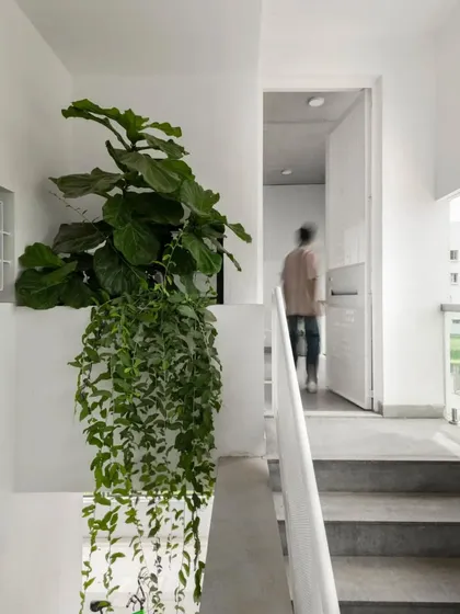 A person walks through the upper floor corridor, demonstrating the human scale of the space. The minimalist design with white walls and simple railings keeps the focus on the home's spatial quality and light.