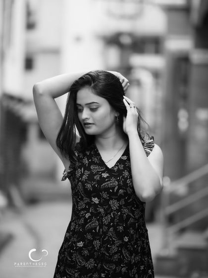 A quiet, introspective moment in a city lane. The black and white conversion adds a sense of nostalgia and focuses on her gentle, downward gaze.