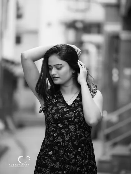 A quiet, introspective moment in a city lane. The black and white conversion adds a sense of nostalgia and focuses on her gentle, downward gaze.