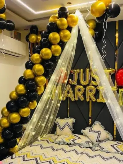 I can transform a bedroom into a romantic space for a "Just Married" couple or a special surprise. This decoration includes a beautiful canopy made of sheer fabric and fairy lights over the bed, paired with "Just Married" foil balloons and a black and gold balloon garland.