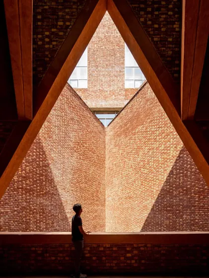 A triangular window frames a view of the brick facade, showcasing the project's masterful use of geometry and light.
