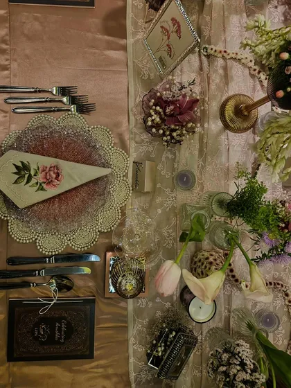 An overhead view of an exquisite table setting I designed for an intimate birthday dinner. The design layers textures and soft colors, from the pink glass charger plates and floral-printed napkins to the delicate flowers and personalized menus, creating a truly bespoke dining experience.