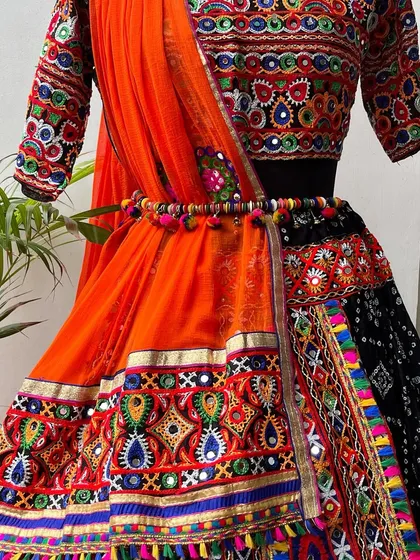 A close-up of this black and red chaniya choli. The orange dupatta adds a bright pop of color, and the pom-pom belt is a fun detail.