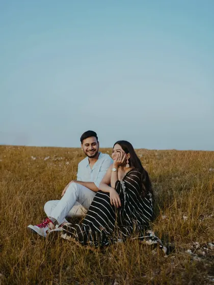 A relaxed moment in the hills of Udaipur. The couple shares a laugh while sitting in a field of golden grass, showcasing the fun and easygoing side of their relationship.
