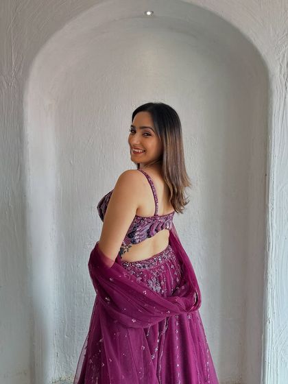 A smiling shot showcasing the back of the stylish velvet blouse. The tassel details add a playful touch to this elegant lehenga.