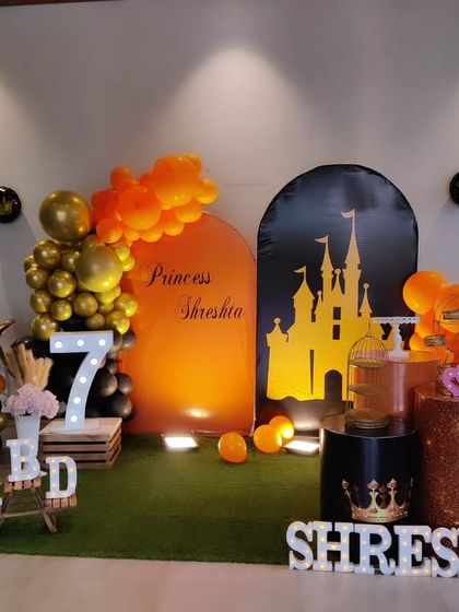 A unique princess-themed seventh birthday with a black and orange color scheme. The setup features a castle silhouette backdrop and a large light-up number '7'.
