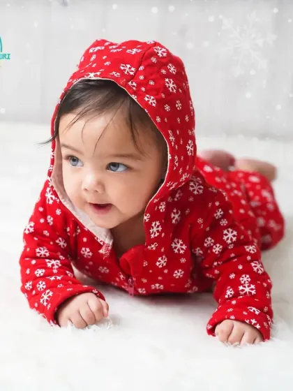 A sweet smile from one of the twin girls during their six-month milestone session. The snowy white background makes her red outfit pop.