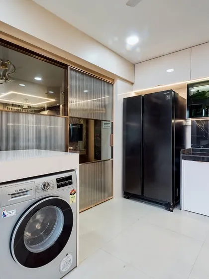 Another view of the utility and kitchen area, showing the side-by-side refrigerator and the washing machine neatly placed. The design ensures that even practical areas of the home look good.