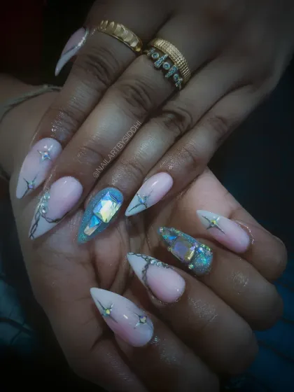 Sharp stiletto nails featuring a mix of delicate line work and bold, chunky iridescent crystals for a showstopping effect.