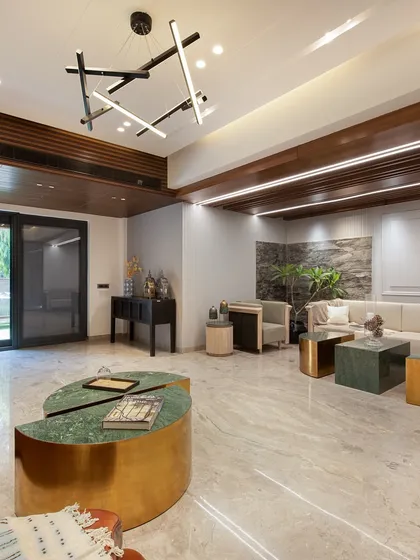 This living area combines a modern leather sofa with a custom-designed green marble and brass coffee table. A contemporary chandelier and wooden ceiling details add layers of texture and sophistication.