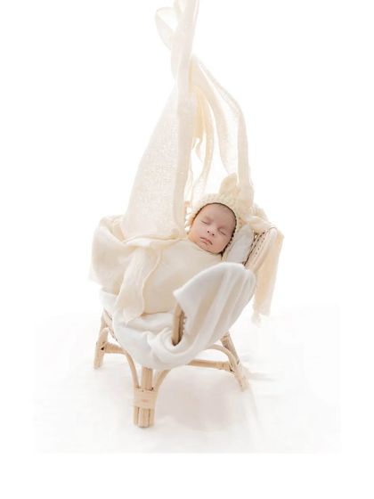 A newborn sleeps in a charming miniature rocking chair, draped with soft fabrics. This creative setup adds a touch of rustic charm to the newborn session, resulting in a unique and sweet image.