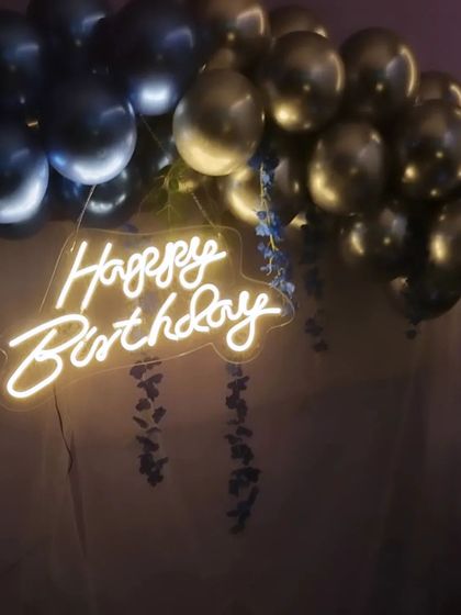 A close-up of the 'Happy Birthday' neon sign against a backdrop of dark blue and silver balloons. I also added some hanging floral elements for a more delicate touch.