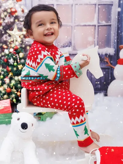 A happy toddler in a Christmas sweater, smiling brightly while riding a rocking horse in a winter wonderland.
