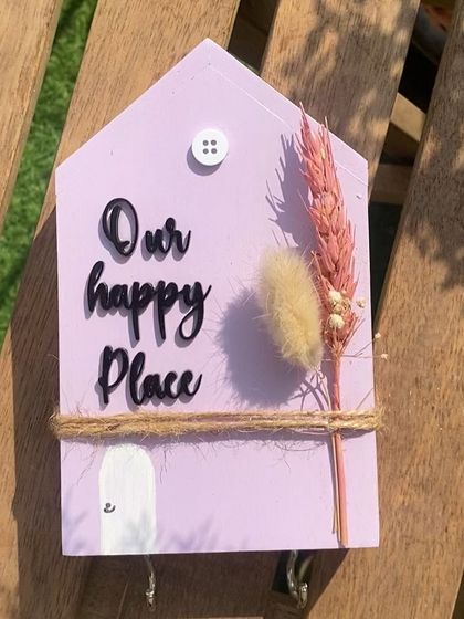 The finished "Our Happy Place" key holder, a charming and useful accessory for your entryway. The combination of the pastel paint, natural twine, and dried flowers gives it a lovely rustic feel.