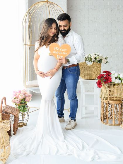 A beautiful couple's portrait in our bright boho studio. They hold a heart-shaped sign that reads "We can't wait to see you," adding a personal and heartfelt touch.