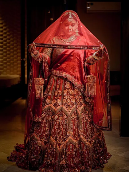 A full-length portrait capturing a traditional moment of a bride with her veil, showcasing the entire lehenga.