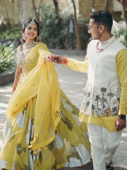 A candid walking shot that captures the flow of the bride's lehenga and the couple's connection. Her makeup looks effortless and radiant.