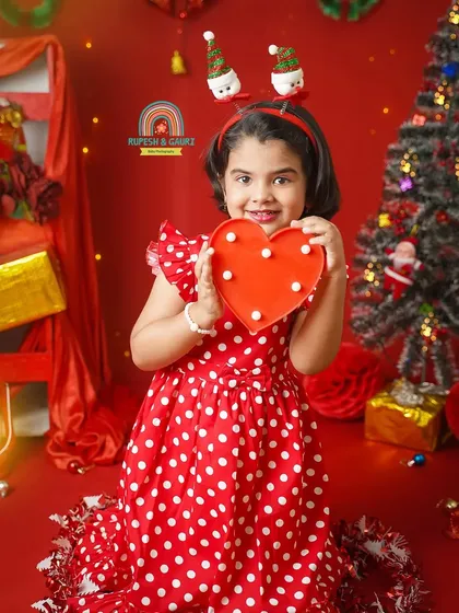 A little girl in a red polka-dot dress holds a heart, surrounded by the warm glow of our Christmas decorations.