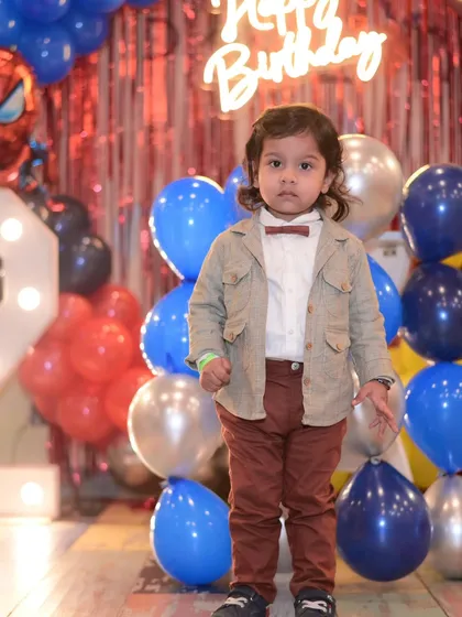 Our little hero standing proudly at his Spiderman-themed 2nd birthday party. The red and blue balloon decor and light-up number "2" make it extra special.