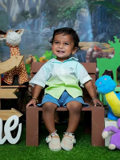 Welcome to the jungle. This first birthday shoot has a fun animal theme, with lots of plush toys, a jungle backdrop, and a happy one-year-old enjoying the setup.