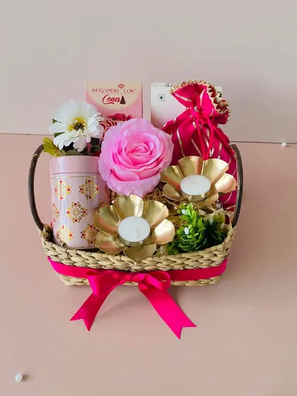 This Kauna basket with a handle is curated with a pink theme. It includes a decorative tin, golden T-light holders, and a pink potli.