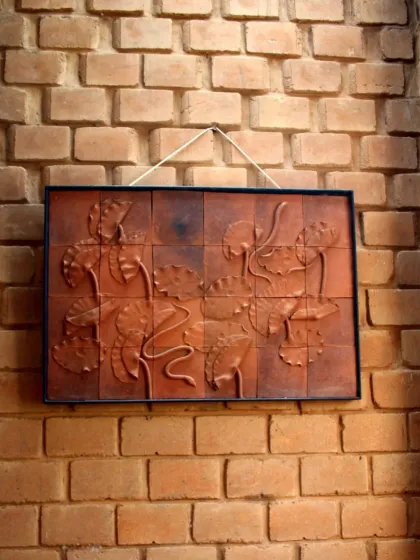A framed terracotta tile relief of lotus flowers hung on a textured brick wall. This shows how we appreciate and incorporate art at every scale, from large murals to smaller, curated pieces.