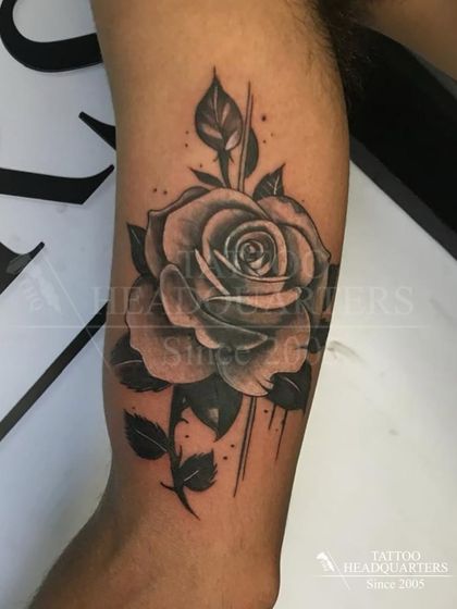 A large, beautifully shaded black and grey rose tattoo on the forearm, showcasing detailed petal work.