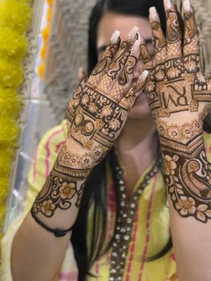 A full view of a stunning engagement mehndi, with couple's initials 'RM' and intricate paisley and floral patterns extending up the arm.
