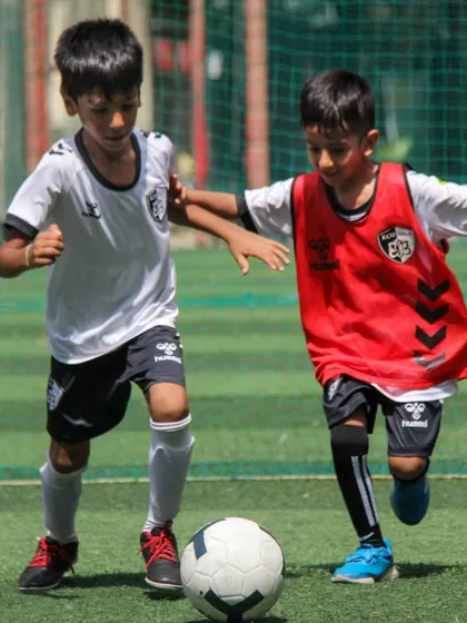 A young player in a red bib battles for possession, showing the fight and resilience we encourage in every match.