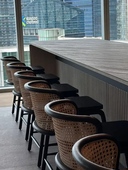 A set of custom bar stools designed for a corporate lounge overlooking the city. These stools feature a dark wood finish and intricate cane backrests, combining durability for high-traffic areas with a sophisticated aesthetic.