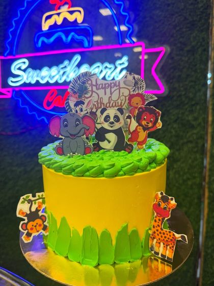 A jungle theme cake full of cute animals like an elephant, panda, and lion. The bright green and yellow colors create a cheerful and wild setting for a fun birthday party.