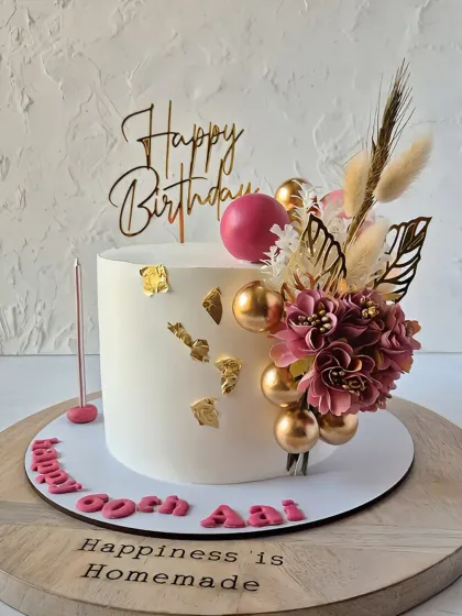 A classic white cake adorned with a beautiful arrangement of dried and paper flowers in shades of pink and gold.