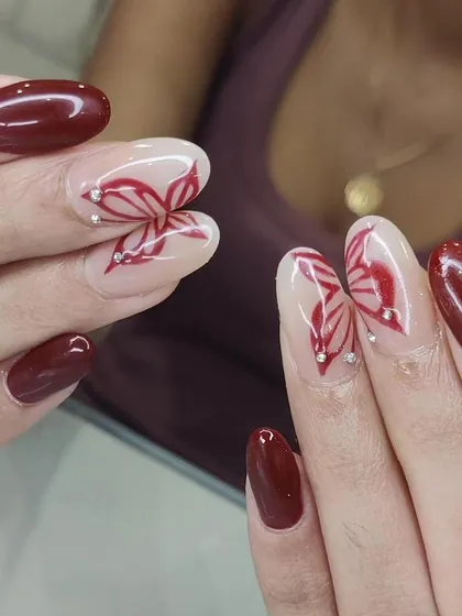 An elegant design with deep red nails and accent nails featuring abstract butterfly wings with rhinestone details.