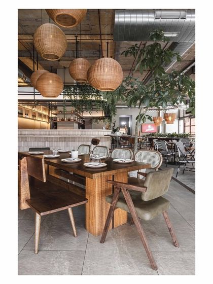 The large wooden community table is paired with a mix of bench and chair seating, offering flexibility. The woven pendant lights above anchor the setting and add a touch of natural, rustic charm.