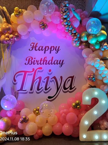 A cute elephant-themed decoration for a 2nd birthday, featuring a pink and gold balloon arch and a light-up number '2'.