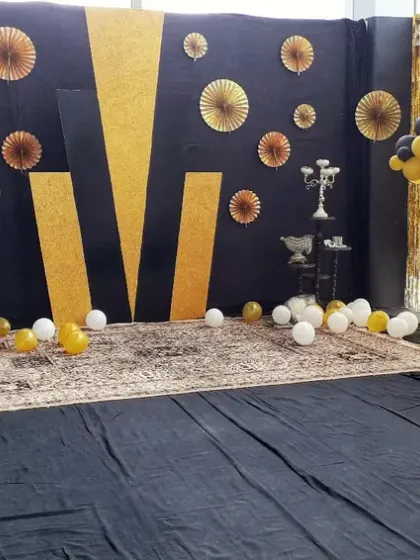For smaller parties or corporate events, I can create custom photo booths or simple stage areas. This black and gold themed setup uses a patterned backdrop, balloon arrangements, and decorative props for a stylish selfie spot.