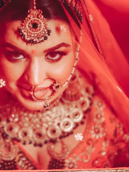 A captivating close-up of a bride under her red veil, looking directly at the camera. The intense red lighting and her expression create a powerful and dramatic portrait.