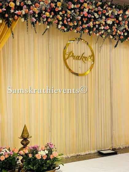 A simple yet elegant engagement backdrop with golden drapes and a personalized name sign. The floral arrangements in shades of pink and peach add a soft, romantic touch.