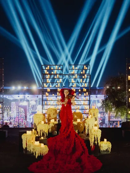 A violinist in a stunning red gown performs amidst a field of molten wax-effect candles and towering candle walls, creating a powerfully dramatic and artistic moment for a wedding reception.