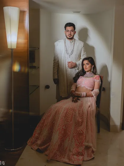 A formal and regal portrait of the couple. The bride is seated while the groom stands behind her, creating a classic composition that exudes elegance and sophistication.