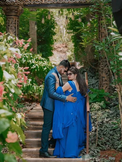 A romantic moment on a staircase surrounded by lush greenery and flowers. The bride's royal blue gown is the centerpiece of this beautiful shot.