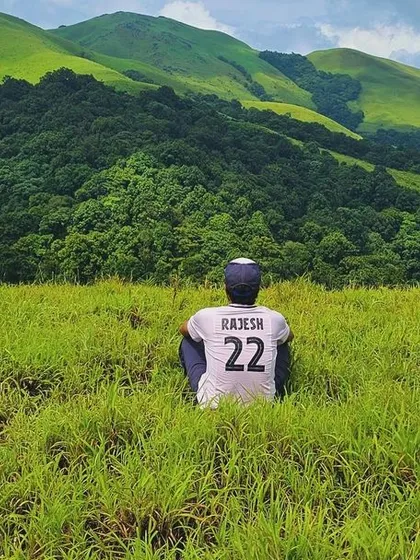 Taking a quiet moment to soak in the view. This photo from the Bandaje trek shows a trekker sitting in a meadow, surrounded by the immense beauty of the Western Ghats.