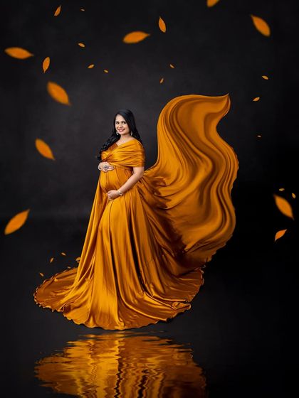A dramatic fabric toss with a golden-yellow gown, enhanced by a water reflection and falling leaves for an autumnal feel.