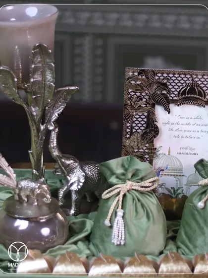 A close-up of a curated hamper, showing a silver elephant figurine, a decorative jar, and a photo frame with a Mughal-inspired design. The rich green velvet and gold accents create a sense of opulence.