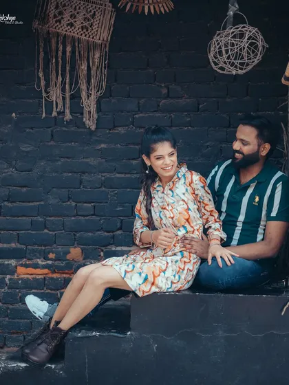 A relaxed and candid moment of the couple sharing a laugh. The rustic, dark brick wall and macrame hangings provide a trendy, bohemian vibe.