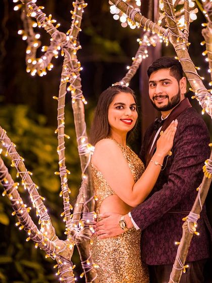 A glamorous couple poses among the fairy-lit trees, with the golden dress shining in the warm light.