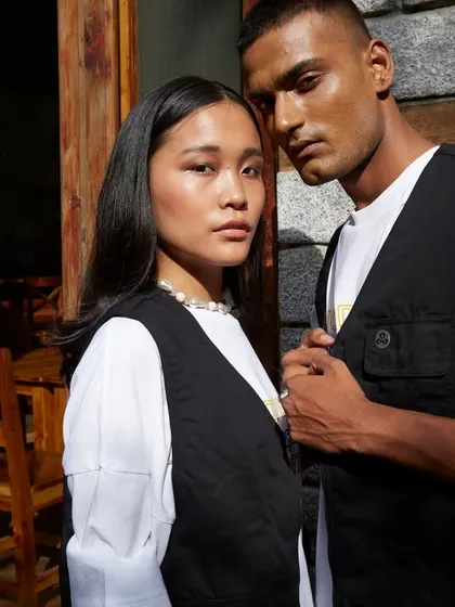 A campaign image for Woodland's "A Skating Monk" collection. The shot captures a quiet, intimate moment between the two models, with the natural light and rustic setting reflecting the brand's connection to nature and urban culture.