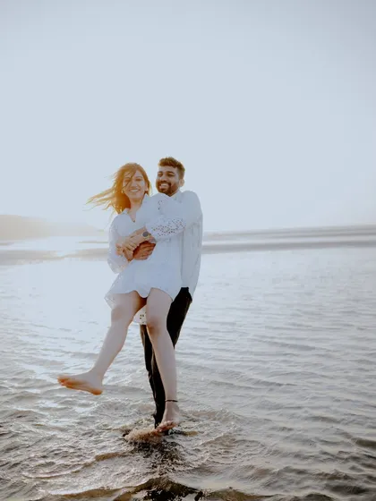 A playful and spontaneous moment captured at the beach. The groom lifting the bride as they stand in the water is full of energy and laughter, showing the fun side of their relationship.