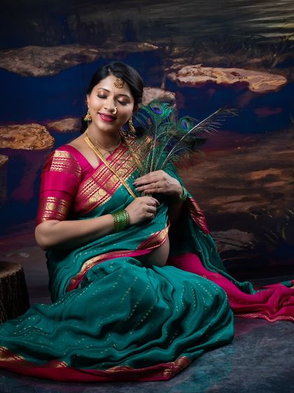A serene moment captured in the studio, with a mother-to-be in a saree holding peacock feathers close to her bump.
