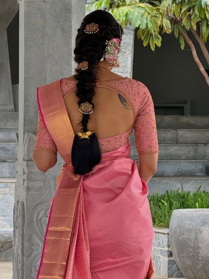 A back view of Shwetha Prasad's lotus pink ensemble, highlighting her traditional braided hairstyle and the keyhole back of the custom blouse.